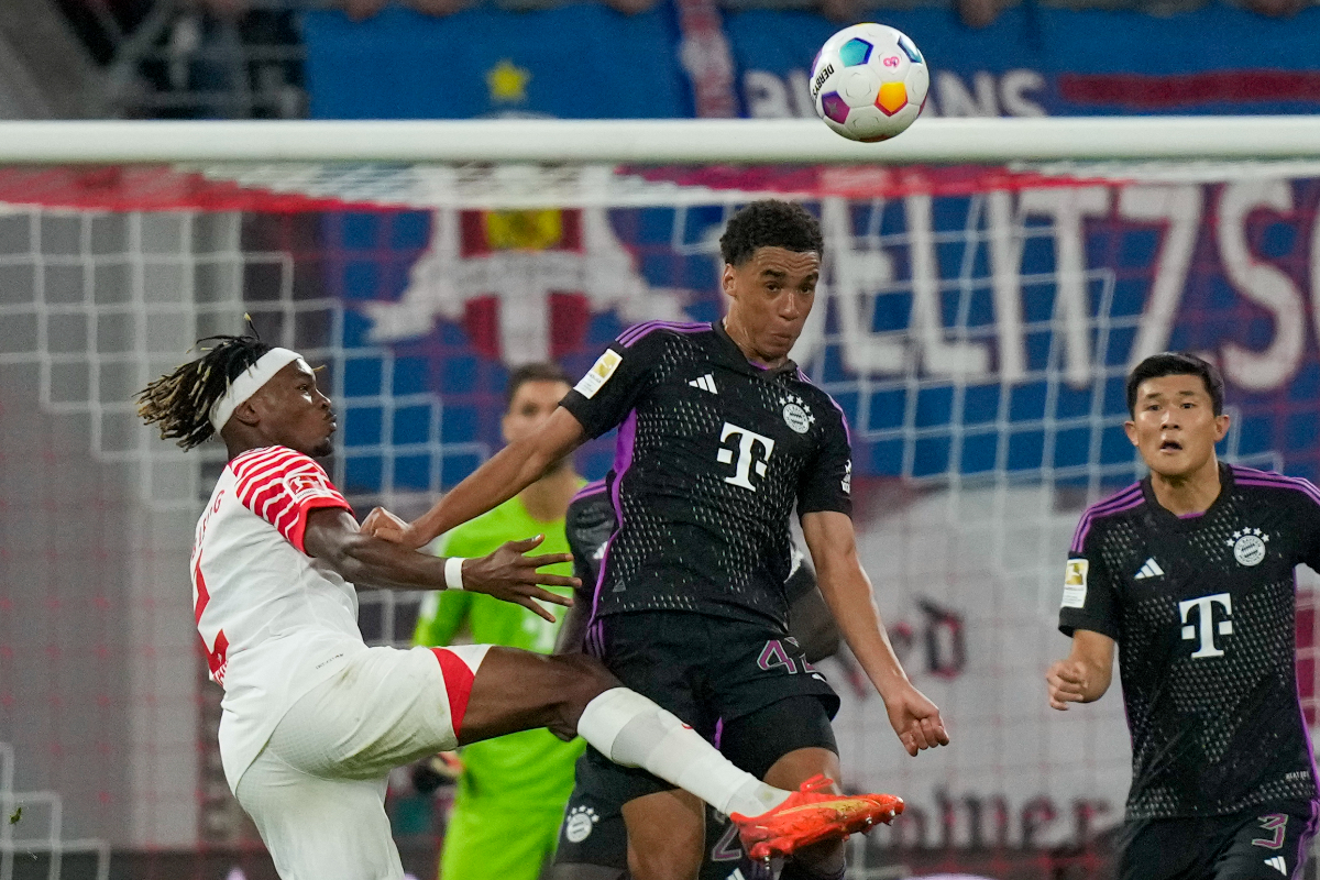 Bayern's Jamal Musiala, center, heads the ball pressured by Leipzig's Mohamed Simakan during the German Bundesliga soccer match between Leipzig and Bayern Munich, at the Red Bull Arena stadium in Leipzig, Germany, Saturday, Sept. 30, 2023. (AP Photo/Matthias Schrader)