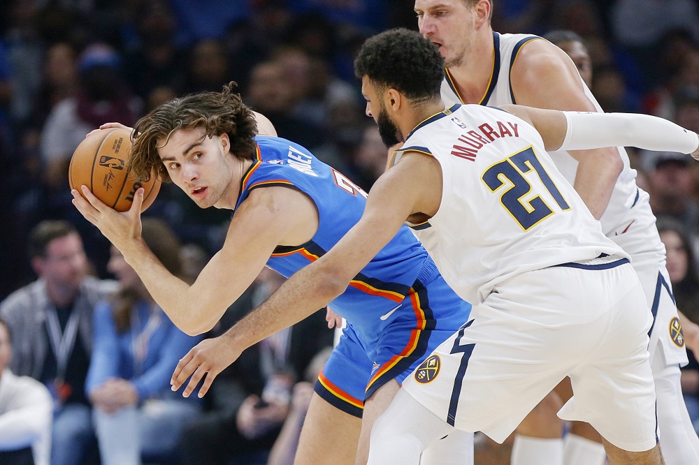 Oklahoma City Thunder guard Josh Giddey, left, holds the ball away from Denver Nuggets guard Jamal Murray (27) and center Nikola Jokic, right, in the first half of an NBA basketball game, Sunday, Oct. 29, 2023, in Oklahoma City. (AP Photo/Nate Billings)
