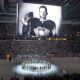 The Pittsburgh Penguins and Anaheim Ducks gather at center ice, before an NHL hockey game in Pittsburgh, Monday, Oct. 30, 2023, to honor former Penguin player Adam Johnson, shown on scoreboard, who died in while playing in an English hockey league game. (AP Photo/Gene J. Puskar)
