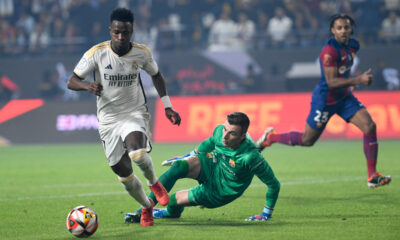 Real Madrid's Vinicius Junior, left, passes through Barcelona's goalkeeper Inaki Pena during the Spanish Super Cup final soccer match between Real Madrid and Barcelona at Al-Awwal Park Stadium in Riyadh, Saudi Arabia, Sunday, Jan. 14, 2024. (AP Photo)