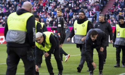 Stewards collect items from the pitch as Bayern goalkeeper Manuel Neuer stands in the background, during the German Bundesliga soccer match between Bayern Munich and Borussia Moenchengladbach, at the Allianz Arena in Munich, Germany, Saturday, Feb. 3, 2024. (Sven Hoppe/dpa via AP)