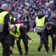Stewards collect items from the pitch as Bayern goalkeeper Manuel Neuer stands in the background, during the German Bundesliga soccer match between Bayern Munich and Borussia Moenchengladbach, at the Allianz Arena in Munich, Germany, Saturday, Feb. 3, 2024. (Sven Hoppe/dpa via AP)