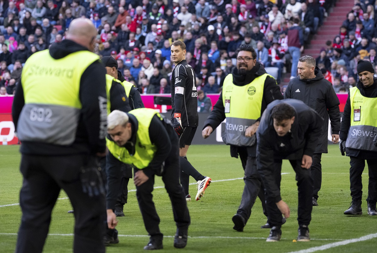 Stewards collect items from the pitch as Bayern goalkeeper Manuel Neuer stands in the background, during the German Bundesliga soccer match between Bayern Munich and Borussia Moenchengladbach, at the Allianz Arena in Munich, Germany, Saturday, Feb. 3, 2024. (Sven Hoppe/dpa via AP)