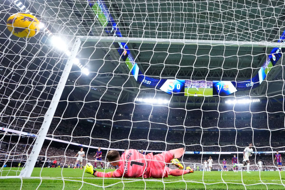 Barcelona's goalkeeper Marc-Andre ter Stegen fails to save the ball as Real Madrid's Vinicius Junior, right, celebrates after scoring his side's opening goal during the Spanish La Liga soccer match between Real Madrid and Barcelona at the Santiago Bernabeu stadium in Madrid, Spain, Sunday, April 21, 2024. (AP Photo/Manu Fernandez)