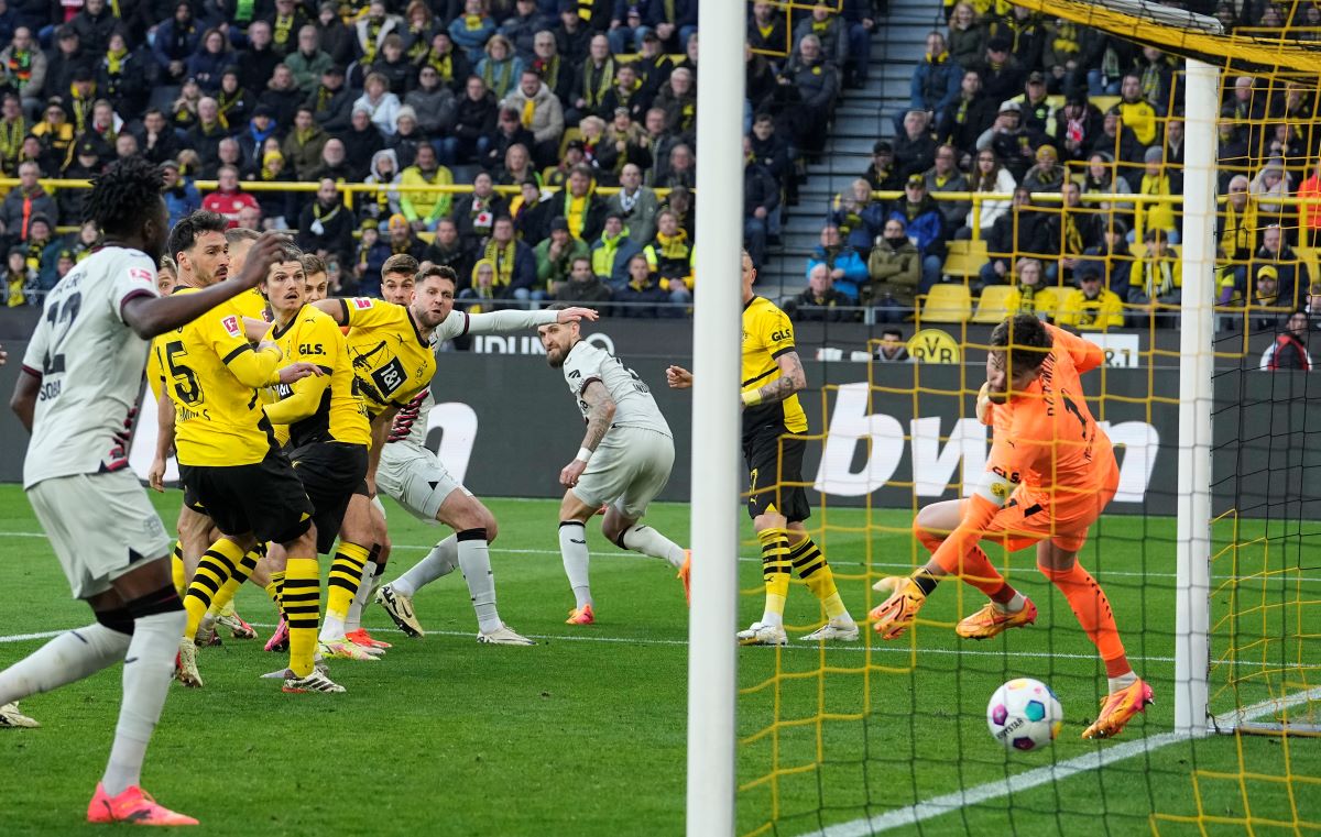 Leverkusen's Josip Stanisic, up, scores for his team in the last minute against Dortmund's goalkeeper Gregor Kobel, right, during the German Bundesliga soccer match between Borussia Dortmund and Bayer Leverkusen in Dortmund, Germany, Sunday, April 21, 2024. The match ended 1-1, Leverkusen is unbeaten since 45 matches. (AP Photo/Martin Meissner)