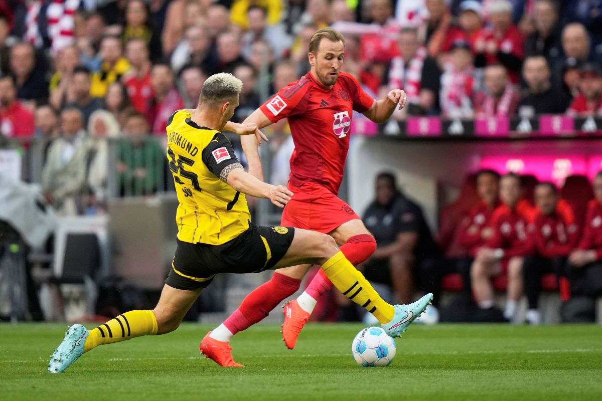 Dortmund's Niklas Suele, bottom left, challenges for the ball with Bayern's Harry Kane during the German Bundesliga soccer match between Bayern Munich and Borussia Dortmund at the Allianz Arena in Munich, Germany, Saturday, April 12, 2025. (AP Photo/Matthias Schrader)