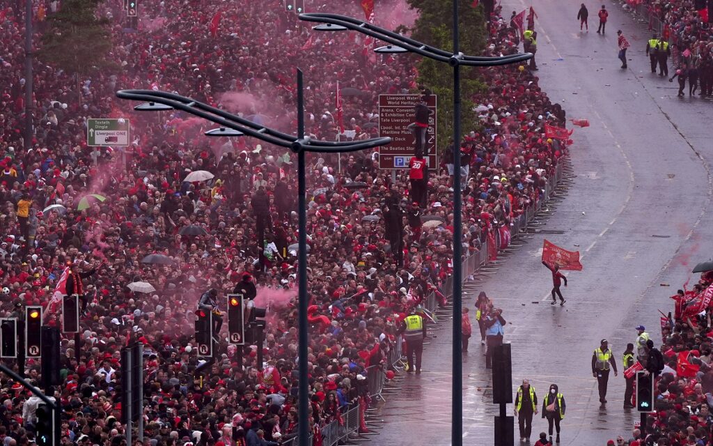 A Liverpool fan running through the streets with a flag near Liverpool Waterfront as people wait for the players during the Premier League winners parade in Liverpool, England, Monday, May 26, 2025. (Owen Humphreys/PA via AP)