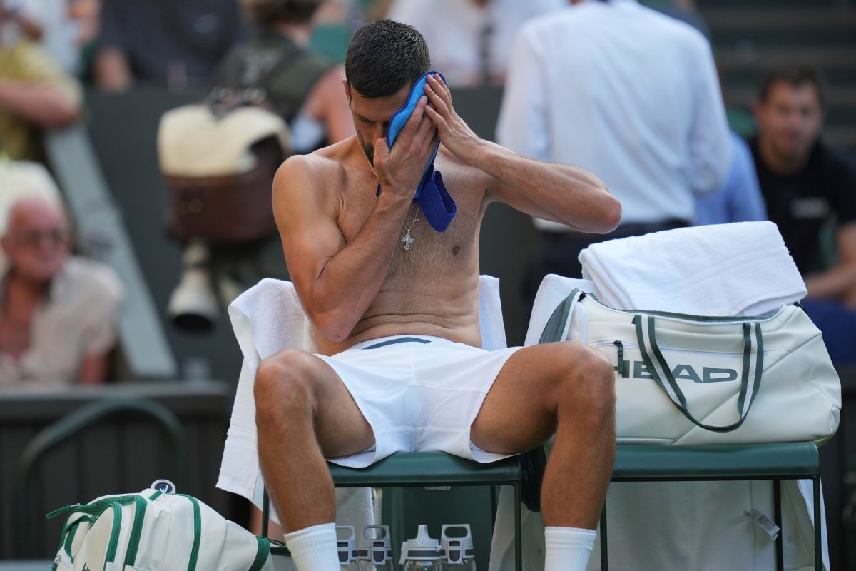 Novak Djokovic of Serbia wipes his face during a break as he plays Alexandre Muller of France during their first round men's singles match at the Wimbledon Tennis Championships in London, Tuesday, July 1, 2025. (AP Photo/Kin Cheung)