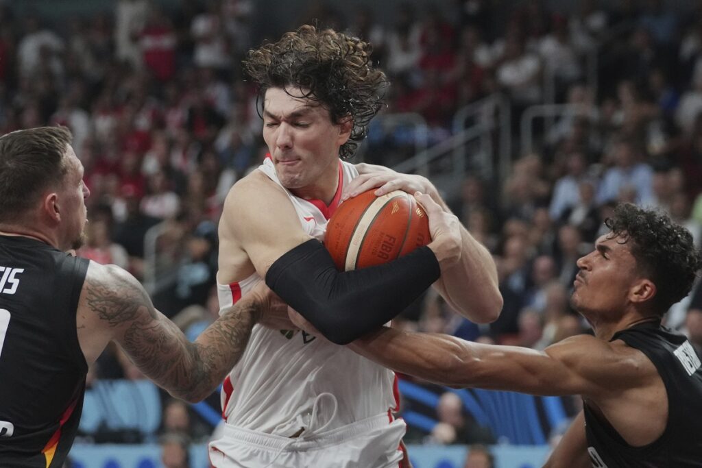 Turkey's Cedi Osman, center, jumps for a lost ball as Germany's Daniel Theis, left, and Tristan Da Silva block him during the Eurobasket, European Basketball Championship final match between Turkey and Germany at the Riga Arena in Riga, Latvia, Sunday, Sept. 14, 2025. (AP Photo/Sergei Grits)