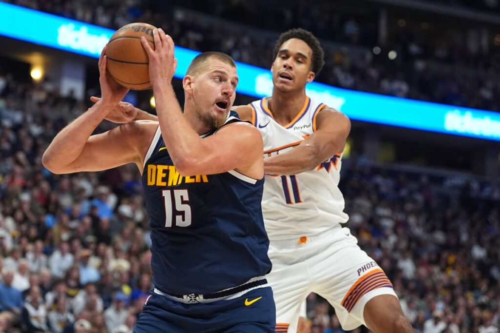 Denver Nuggets center Nikola Jokic, left, pulls in a rebound as Phoenix Suns forward Oso Ighodaro, right, defends in the first half of an NBA basketball game Saturday, Oct. 25, 2025, in Denver. (AP Photo/David Zalubowski)