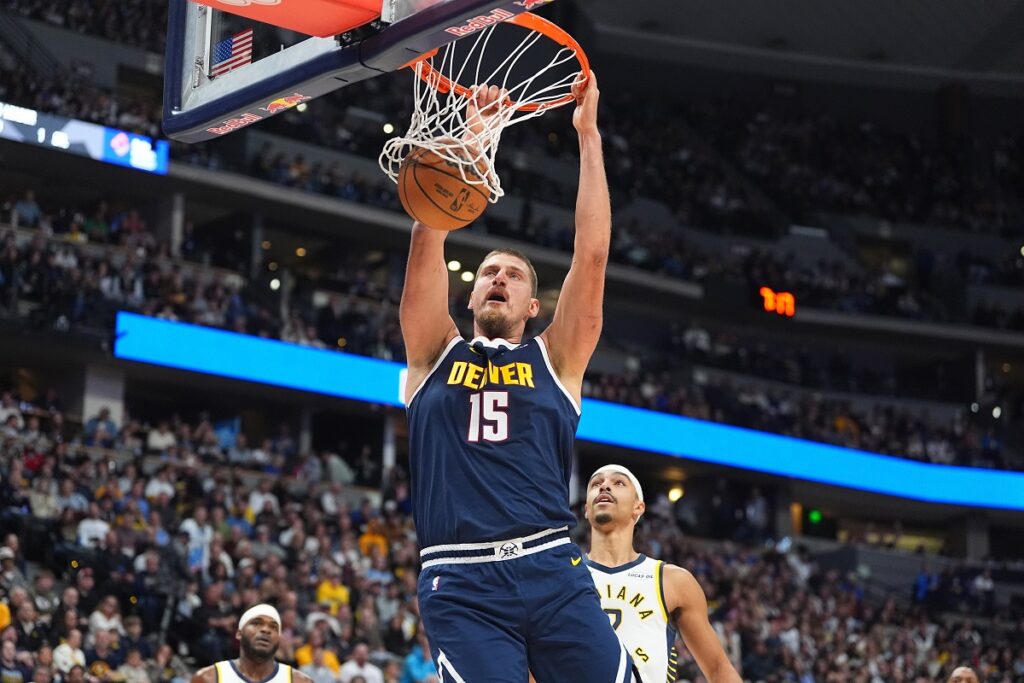 Denver Nuggets center Nikola Jokić, fronbt, dunks the ball for a basket over Indiana Pacers guard/forward Andrew Nembhard in the first half of an NBA basketball game Saturday, Nov. 8, 2025, in Denver. (AP Photo/David Zalubowski)