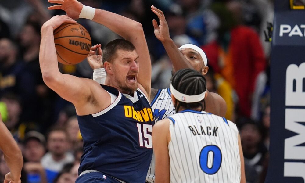 Denver Nuggets center Nikola Jokić, left, pulls in a rebound as Orlando Magic center Wendell Carter Jr., back right, and guard Anthony Black (0) defend in the second half of an NBA basketball game Thursday, Dec. 18, 2025, in Denver. (AP Photo/David Zalubowski)