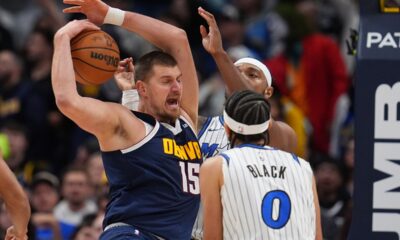 Denver Nuggets center Nikola Jokić, left, pulls in a rebound as Orlando Magic center Wendell Carter Jr., back right, and guard Anthony Black (0) defend in the second half of an NBA basketball game Thursday, Dec. 18, 2025, in Denver. (AP Photo/David Zalubowski)