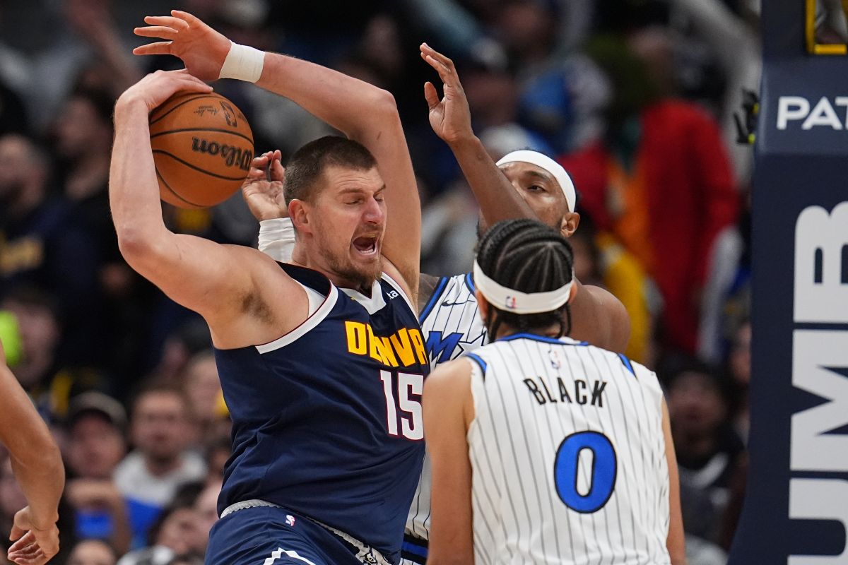 Denver Nuggets center Nikola Jokić, left, pulls in a rebound as Orlando Magic center Wendell Carter Jr., back right, and guard Anthony Black (0) defend in the second half of an NBA basketball game Thursday, Dec. 18, 2025, in Denver. (AP Photo/David Zalubowski)