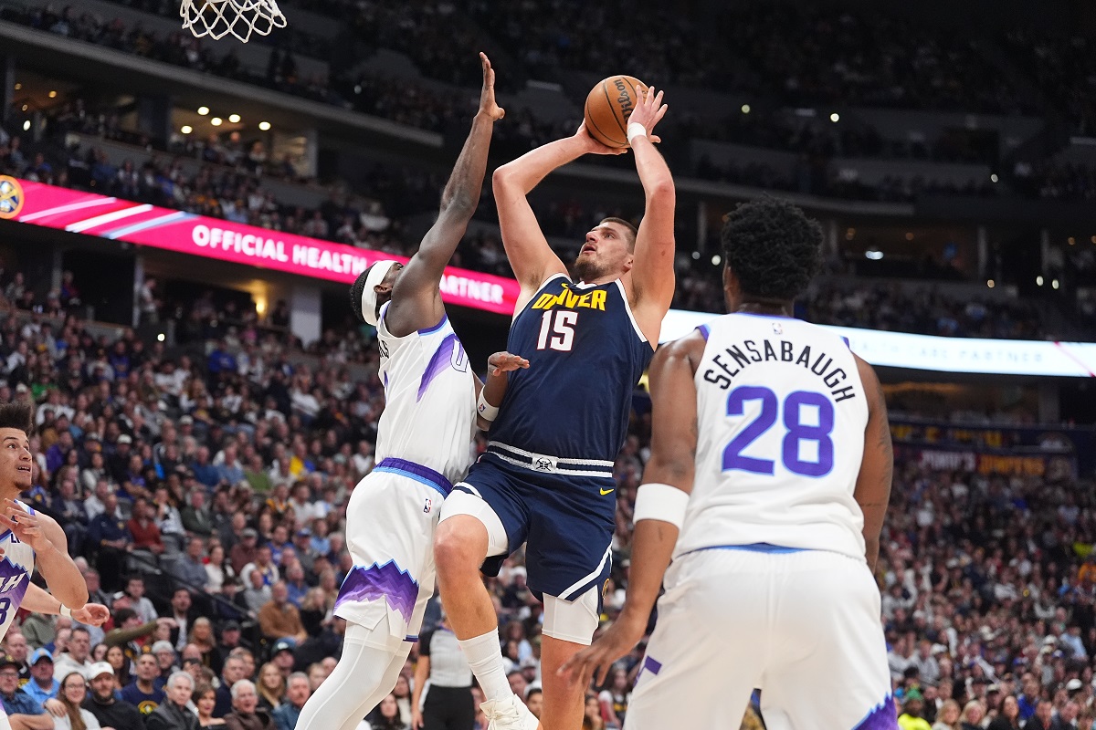 Denver Nuggets center Nikola Jokić, center, drives to the rim between Utah Jazz forwards Taylor Hendricks, left, and Brice Sensabaugh in the first half of an NBA basketball game Monday, Dec. 22, 2025, in Denver. (AP Photo/David Zalubowski)