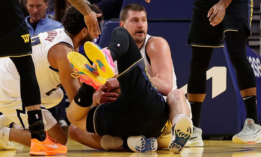 Golden State Warriors guard Brandin Podziemski, center, falls in the lap of Denver Nuggets center Nikola Jokic, center right, before a jump ball is called during the first half of an NBA basketball game, Sunday, Feb. 22, 2026, in San Francisco. (AP Photo/Kelley L Cox)