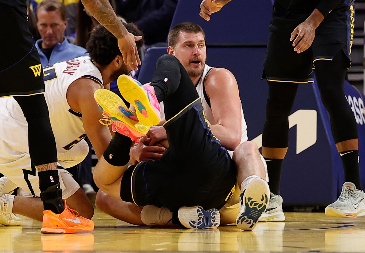 Golden State Warriors guard Brandin Podziemski, center, falls in the lap of Denver Nuggets center Nikola Jokic, center right, before a jump ball is called during the first half of an NBA basketball game, Sunday, Feb. 22, 2026, in San Francisco. (AP Photo/Kelley L Cox)