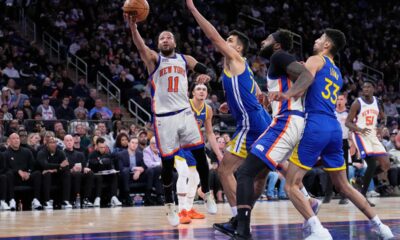New York Knicks' Jalen Brunson (11), left, drives to the basket past Golden State Warriors defenders during the second half of an NBA basketball game Sunday, March 15, 2026, in New York. (AP Photo/Seth Wenig)
