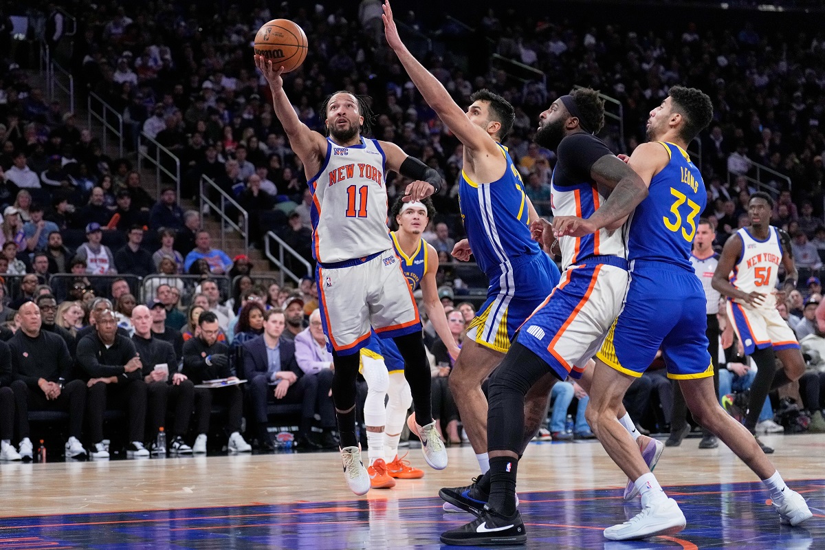 New York Knicks' Jalen Brunson (11), left, drives to the basket past Golden State Warriors defenders during the second half of an NBA basketball game Sunday, March 15, 2026, in New York. (AP Photo/Seth Wenig)