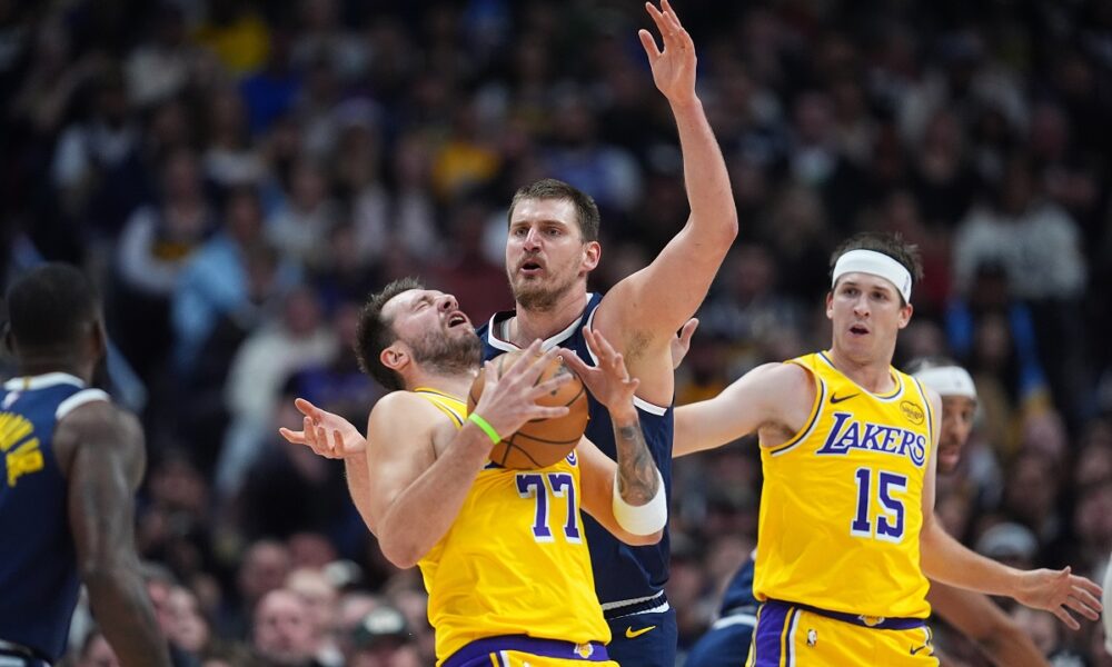 Los Angeles Lakers guard Luka Dončić, left, reacts after getting hit in the face by the ball while fighting for control with Denver Nuggets center Nikola Jokić as Los Angeles guard Austin Reaves, right, looks on in the first half of an NBA basketball game Thursday, March 5, 2026, in Denver. (AP Photo/David Zalubowski)