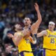 Los Angeles Lakers guard Luka Dončić, left, reacts after getting hit in the face by the ball while fighting for control with Denver Nuggets center Nikola Jokić as Los Angeles guard Austin Reaves, right, looks on in the first half of an NBA basketball game Thursday, March 5, 2026, in Denver. (AP Photo/David Zalubowski)
