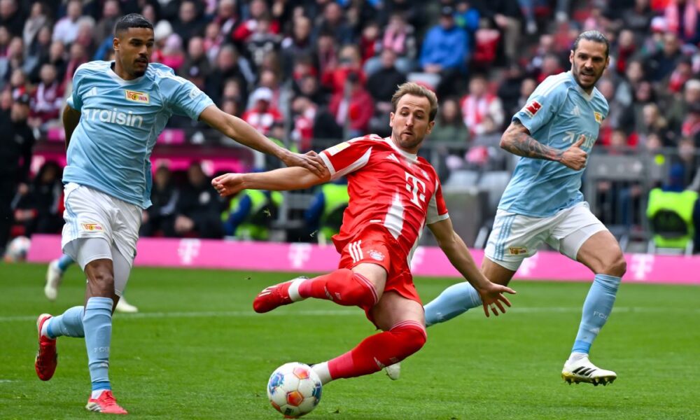 Munich's Harry Kane, center, and Berlin's Livan Burcu, left, challenge for the ball during the German Bundesliga soccer match between FC Bayern Munich and 1. FC Union Berlin in Munich, Germany, Saturday, March 21, 2026 (Sven Hoppe/dpa via AP)