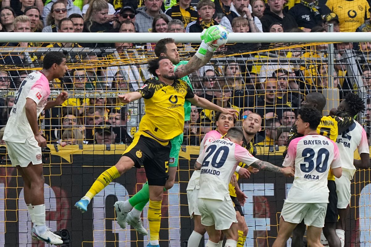 Leverkusen's goalkeeper Mark Flekken catches the ball as he challenges with Dortmund's Ramy Bensebaini during the German Bundesliga soccer match between Borussia Dortmund and Bayer Leverkusen in Dortmund, Germany, Saturday, April 11, 2026. (AP Photo/Martin Meissner)