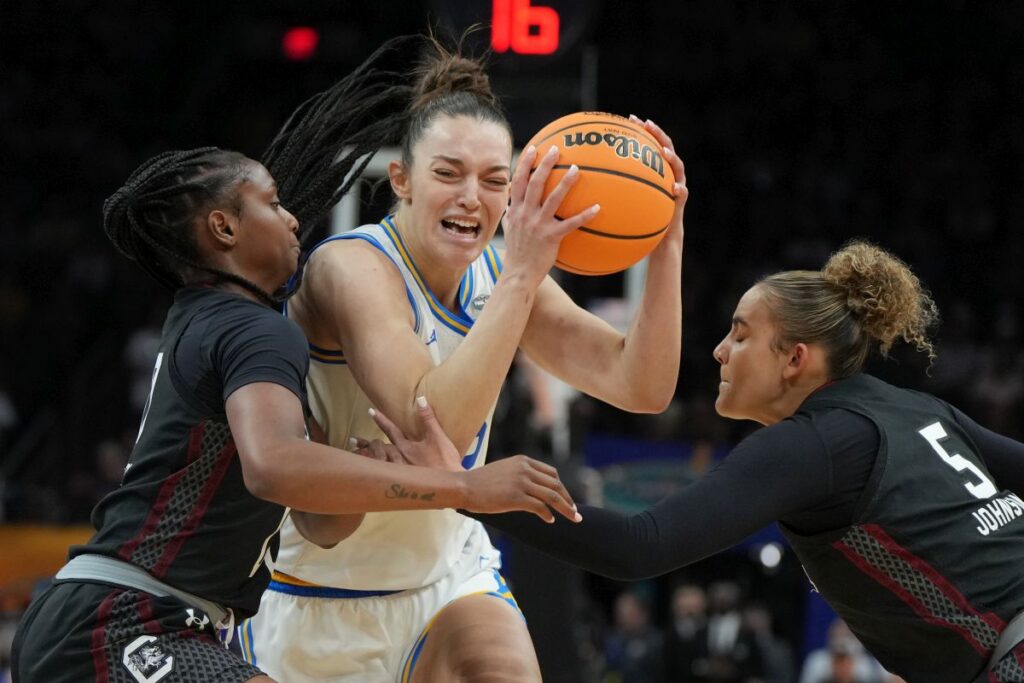 UCLA forward Angela Dugalic (32) drives against South Carolina guard Ta'Niya Latson, left, and South Carolina guard Tessa Johnson (5) during the second half of the women's National Championship Final Four NCAA college basketball tournament game, Sunday, April 5, 2026, in Phoenix. (AP Photo/Rick Scuteri)