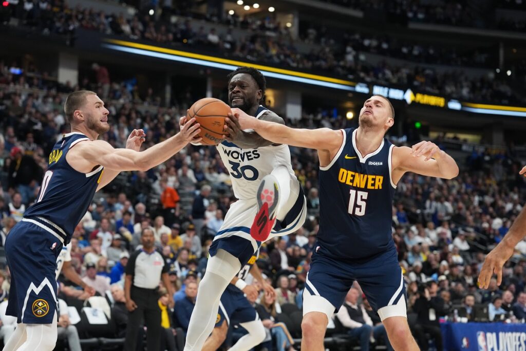 Minnesota Timberwolves forward Julius Randle, center, fights for control of the ball while driving between Denver Nuggets guard Christian Braun, left, and center Nikola Jokic in the second half in Game 5 of a first-round NBA playoffs basketball series Monday, April 27, 2026, in Denver. (AP Photo/David Zalubowski)