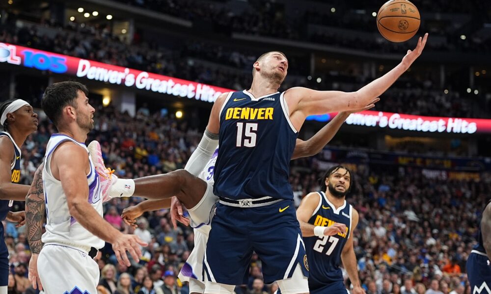 Denver Nuggets center Nikola Jokić, front right, pulls in a rebound as Utah Jazz center Oscar Tshiebwe, back right, and guard John Konchar defend in the second half of an NBA basketball game Friday, March 27, 2026, in Denver. (AP Photo/David Zalubowski)