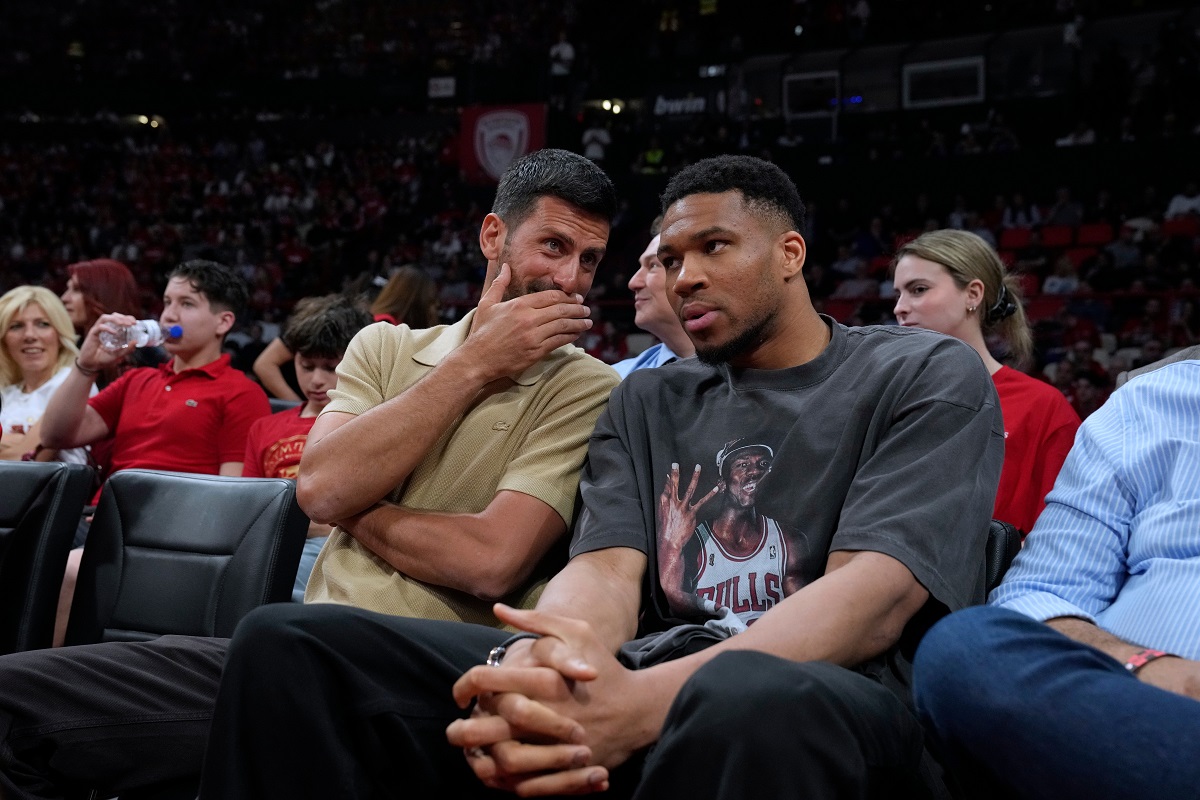 Tennis star Novak Djokovic, left, speaks with Giannis Antetokounmpo of the Milwaukee Bucks while watching a EuroLeague playoffs basketball game between Olympiacos and AS Monaco in Piraeus near Athens, Thursday, April 30, 2026. (AP Photo/Petros Giannakouris)